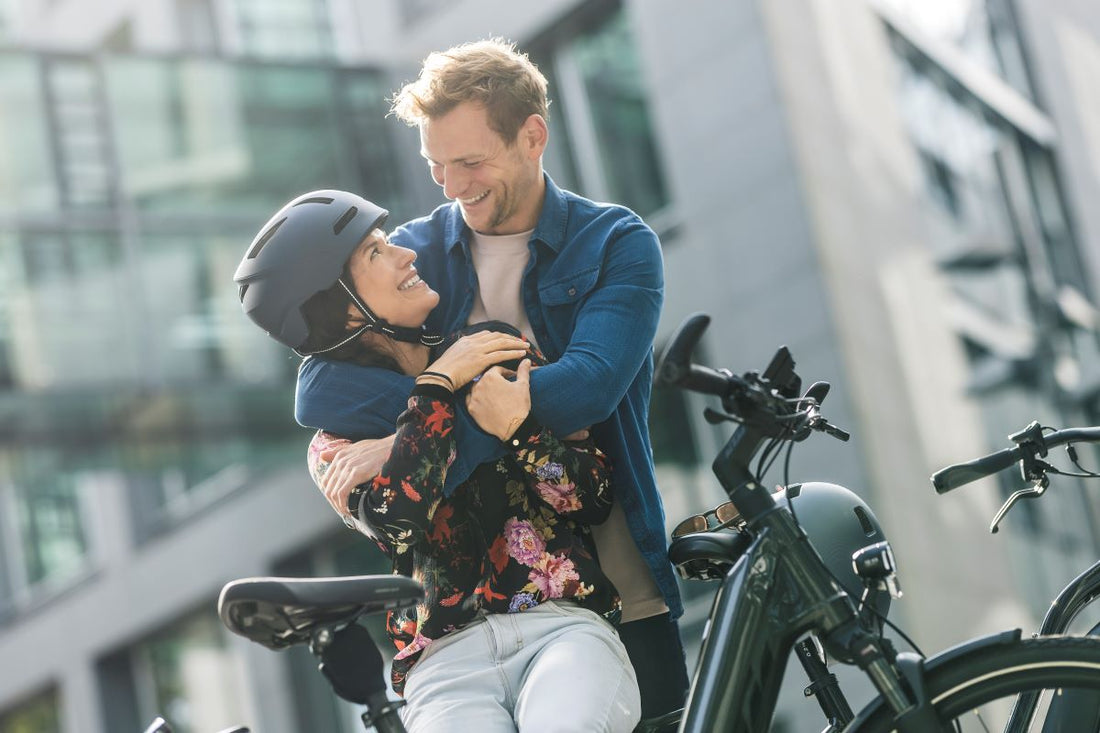 Ein Pärchen, Mann und Frau, stehen bei einem E-Bike in der Stadt und freuen sich.